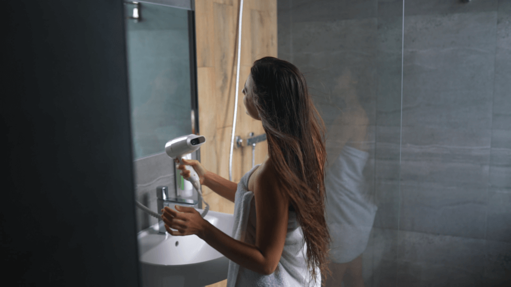 Woman drying hair with blow dryer in bathroom.